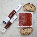 Fermin salami and pepperoni on a wooden surface with packaging.