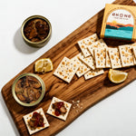 Wooden board with crackers, dips, and a box of ekone oysters on a white background
