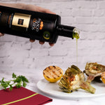 Olive oil being poured from a bottle onto roasted vegetables on a white plate.