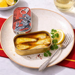 Open can of sardines on a plate with lemon and parsley, next to a PortHos can opener.