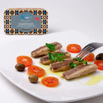 Sardines on a plate with tomatoes and olives, branded container in the background