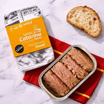 Tuna fillets with fennel in a can on a red napkin with packaging and bread in the background.