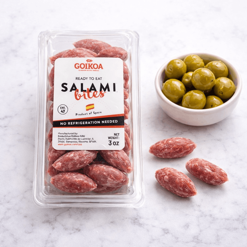 Packaged salami bites with a bowl of green olives on a marble surface