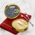 Two open tins of Los Peperetes seabass in albarino sauce on a red napkin with forks on a white marble surface.