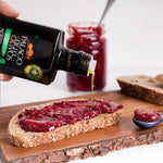 Olive oil being drizzled onto a slice of bread with jam, with a jar of jam and a bottle of Palacio de Olivos olive oil in the background.