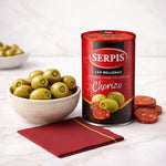 Can of Serpis green olives with chorizo next to a bowl of olives on a white surface