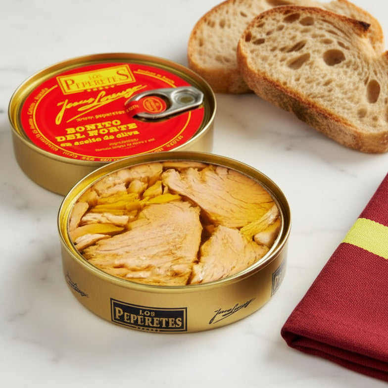 A tin can of Los Peperetes Bonito del Norte white tuna in olive oil, with the tuna visible inside the open can, placed on a textured surface.