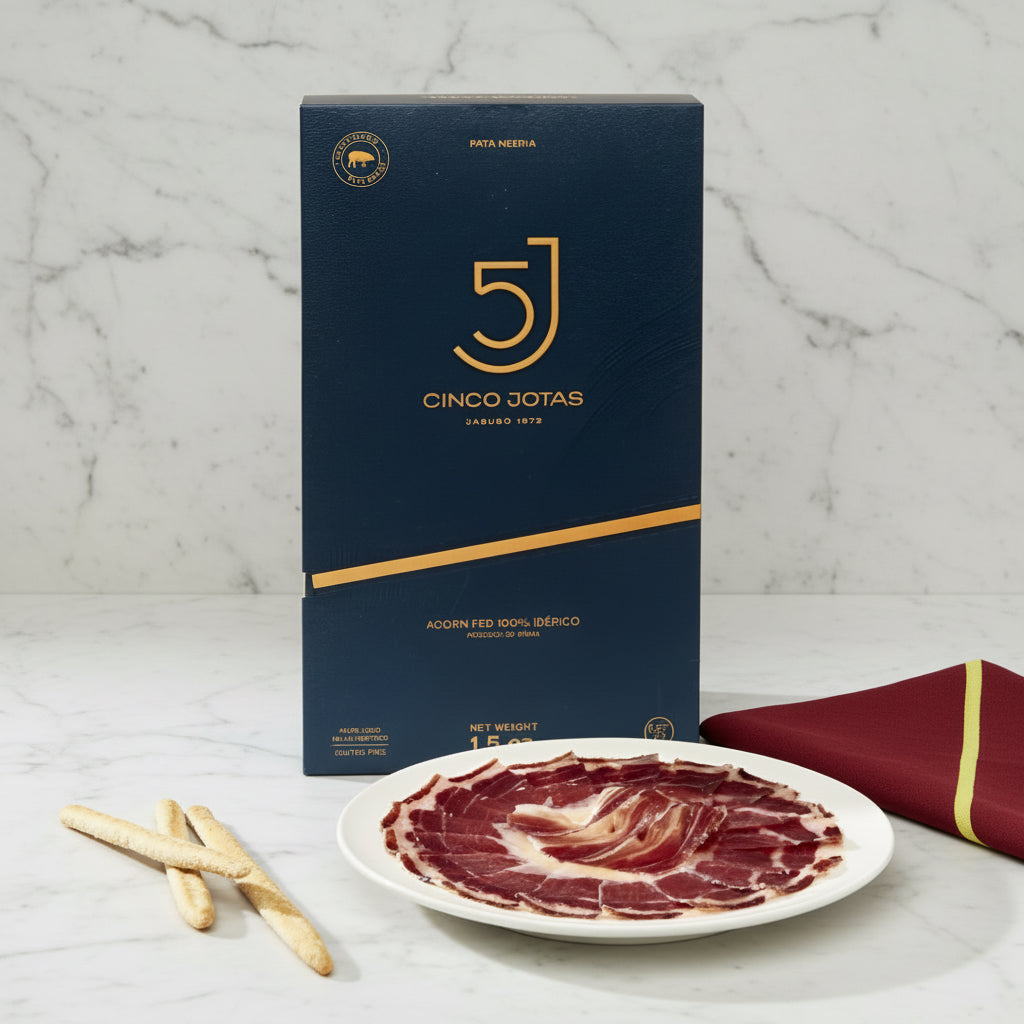 Cinco Jotas packaging with a plate of sliced iberico ham on a neutral background