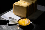 Block of jersey butter on a cutting board with a knife, on a dark surface