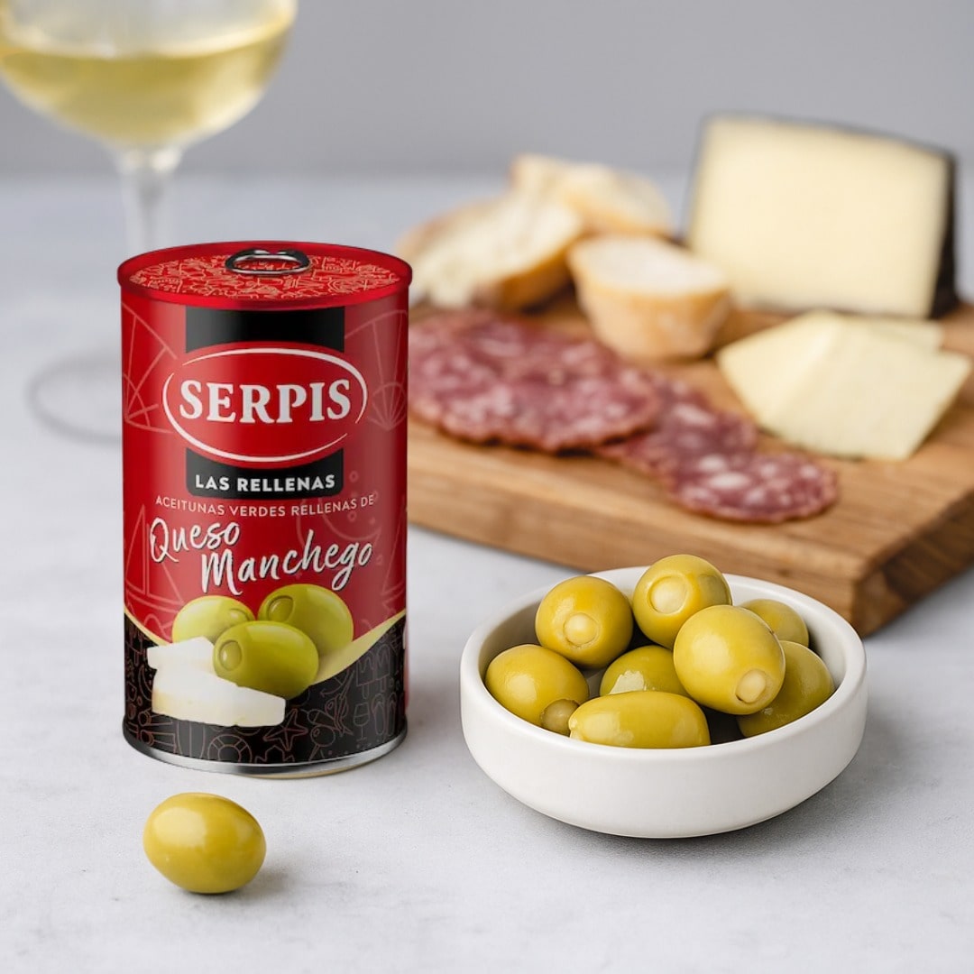 Can of Serpis olives with a bowl of olives and charcuterie on a table