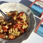 Pasta dish with a fork in a bowl next to Ekone mussels in marinara sauce packaging
