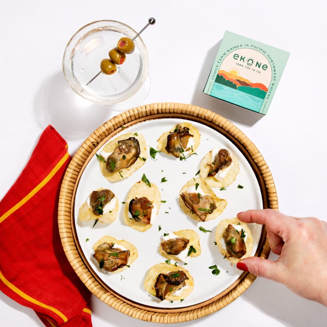 Platter of smoked oysters with a glass of water and Ekone packaging on a white surface