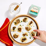 Platter of smoked oysters with a glass of water and Ekone packaging on a white surface