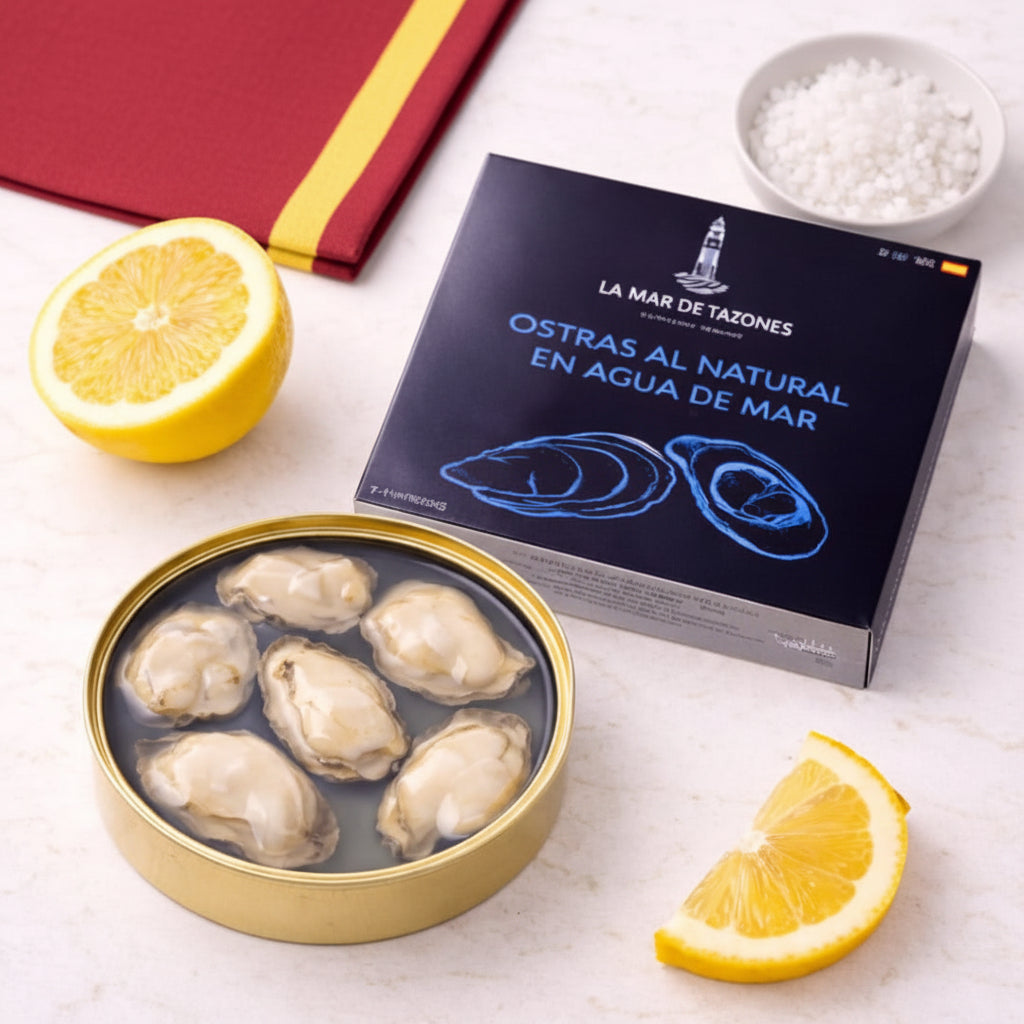 Oysters in a tin with a box labeled 'La Mar de Tazones' on a white surface with lemon slices and salt.