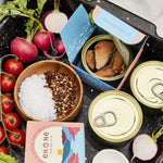 Canned food items on a tray with radishes, tomatoes, and a box of Ekone tea.