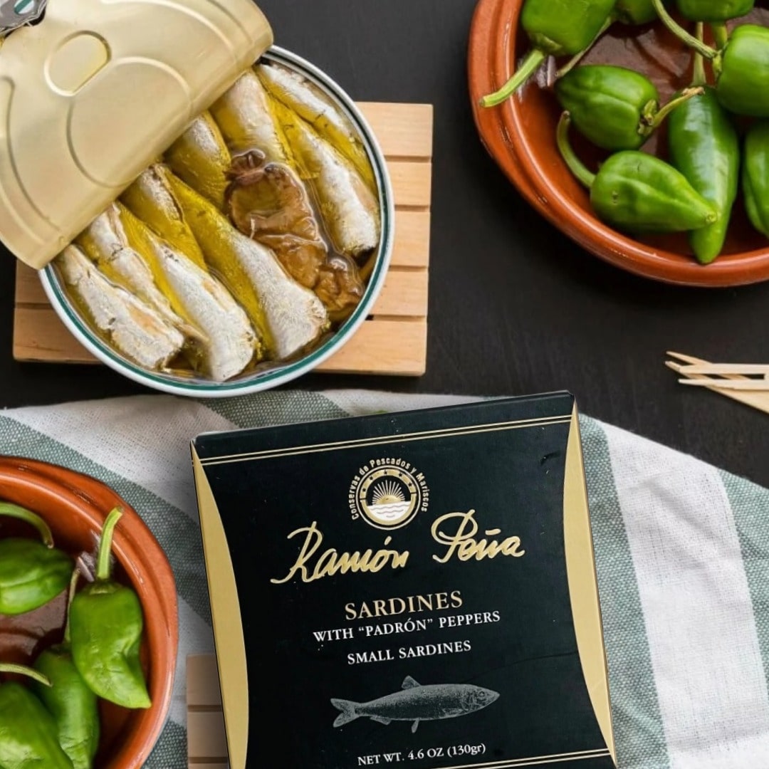 Packaged sardines with pimientos on a table with fresh pimientos.